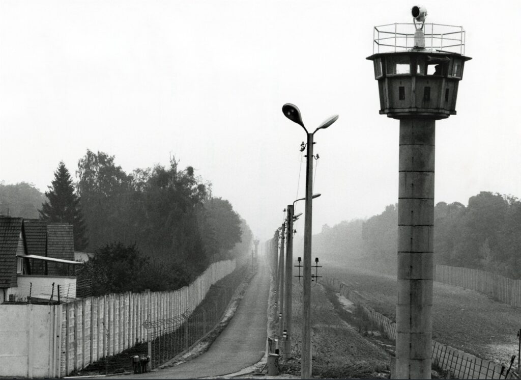 Schwarzweiß Foto, das die Grenzanlagen der ehemaligen innerdeutschen Grenze mit einem Wachturm zeigt.