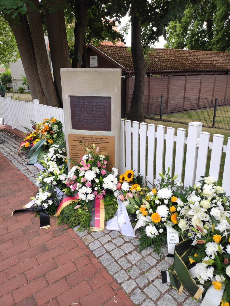 Gedenkstein, an dem mehrere Blumenkränze abgelegt wurden