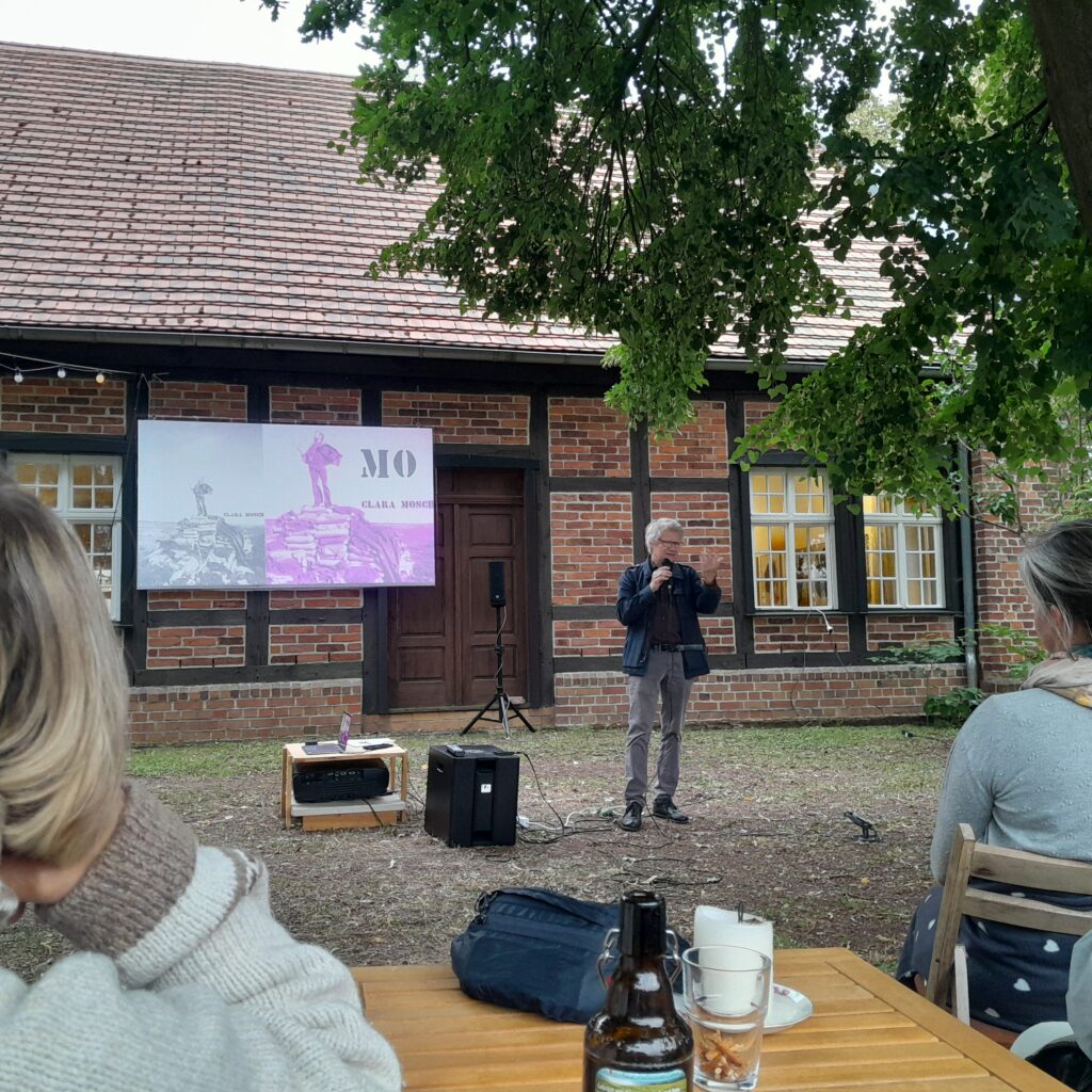 Mann spricht mit Mikrofon spricht vor Filmleinwand zu Publikum